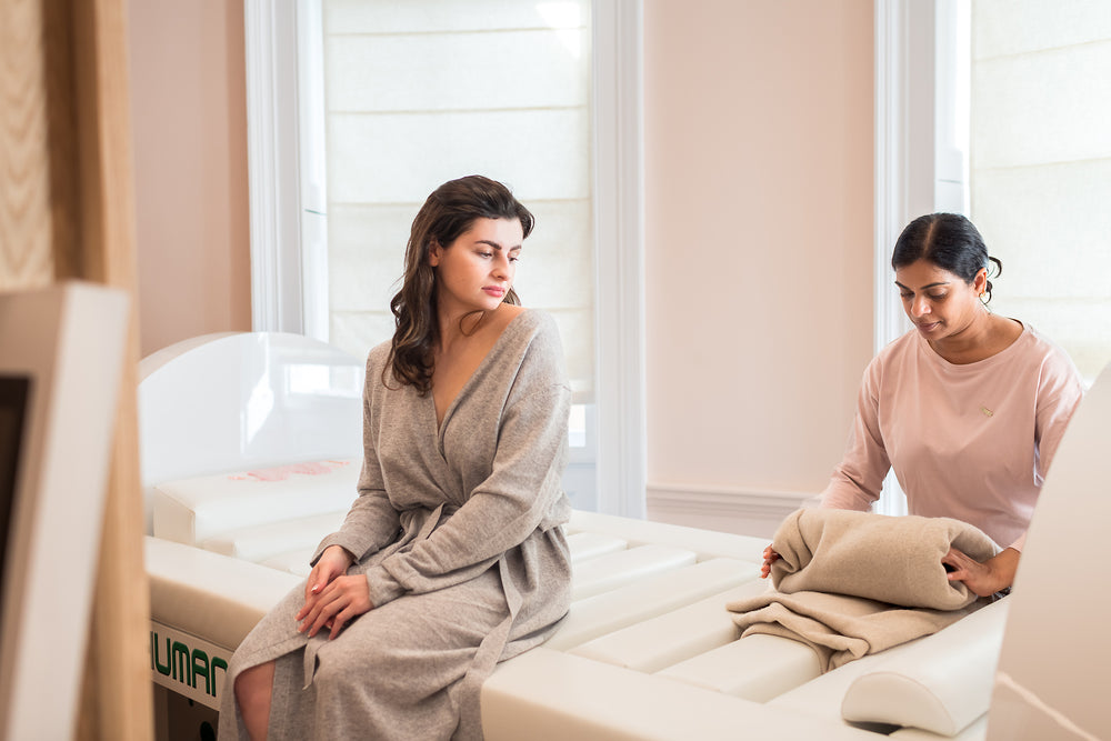 Wellness practitioner preparing a treatment bed while a client relaxes before a personalized RegenX therapy session.